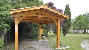 Una struttura in legno a pergola in un giardino con un barbecue sottostante.