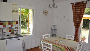 Una cucina con mobili bianchi, zoccolo in piastrelle, una finestra vista verdeggiante, un tavolo da pranzo con sedie e un lampadario.