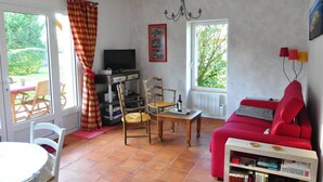 Un soggiorno con un divano rosso, sedie di legno, un tavolo, una televisione e una libreria.
