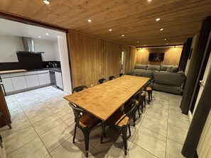 Ein geräumiger Essbereich mit einem langen Holztisch und Stühlen, eine Küche mit modernen Geräten und ein gemütlicher Wohnbereich mit Sofa und Fernseher.
