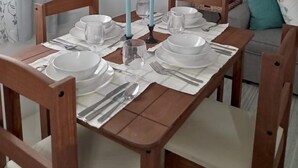 A dining area with a wooden table set for four, surrounded by chairs. There are two candles on the table, and a grey sofa with a teal pillow in the background. - Shirley's Retreat, serenity and charm in a rural setting, 15 mins from airport. (Centeno)