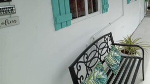 A white building with turquoise shutters and a black metal bench with striped cushions. - Shirley's Retreat, serenity and charm in a rural setting, 15 mins from airport. (Centeno)
