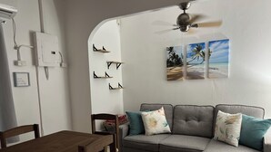 A living room with a gray sofa, a wooden dining table, and a ceiling fan. - Shirley's Retreat, serenity and charm in a rural setting, 15 mins from airport. (Centeno)