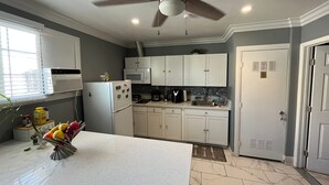 Una cocina con armarios blancos, microondas, refrigerador y ventilador de techo.