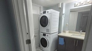 A compact laundry room with two stacked washing machines, a sink with a mirror, and a tiled floor.