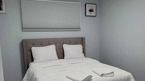 A neatly made bed with white linens and pillows, a headboard with a tufted design, and a ceiling light fixture.