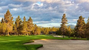 Een golfbaan met een clubhuis, omringd door hoge bomen en bergen op de achtergrond.