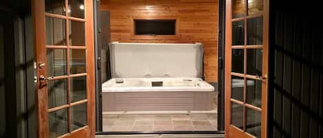 An outdoor hot tub with a wooden bench in front, surrounded by wooden walls and glass doors.