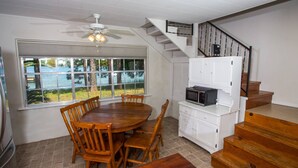 Un coin repas avec une table et des chaises en bois, un ventilateur de plafond et une vue sur un lac, visible à travers de grandes fenêtres.
