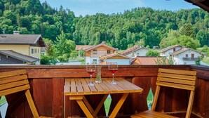 Une terrasse en bois avec une table et des chaises, donnant sur une colline boisée où se trouvent des maisons.