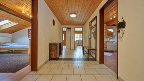 Un couloir avec des poutres en bois au plafond, un sol carrelé et un lit sur le côté gauche.