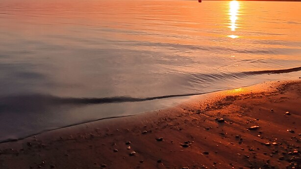 Un coucher de soleil sur une étendue d'eau calme, avec une plage au premier plan.