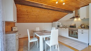Une cuisine moderne avec des meubles blancs, un plafond en bois et un coin repas comprenant une table et des chaises.