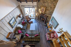 Uma sala de estar aconchegante com lareira, paredes de madeira e um lustre.