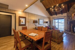 Uma sala de jantar com uma mesa e cadeiras de madeira, uma lareira e vista para as montanhas.