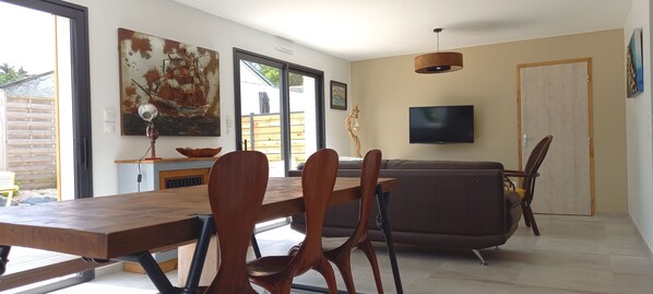 Una sala de estar moderna con una mesa de comedor de madera, un sofá de cuero marrón y un televisor montado en la pared.