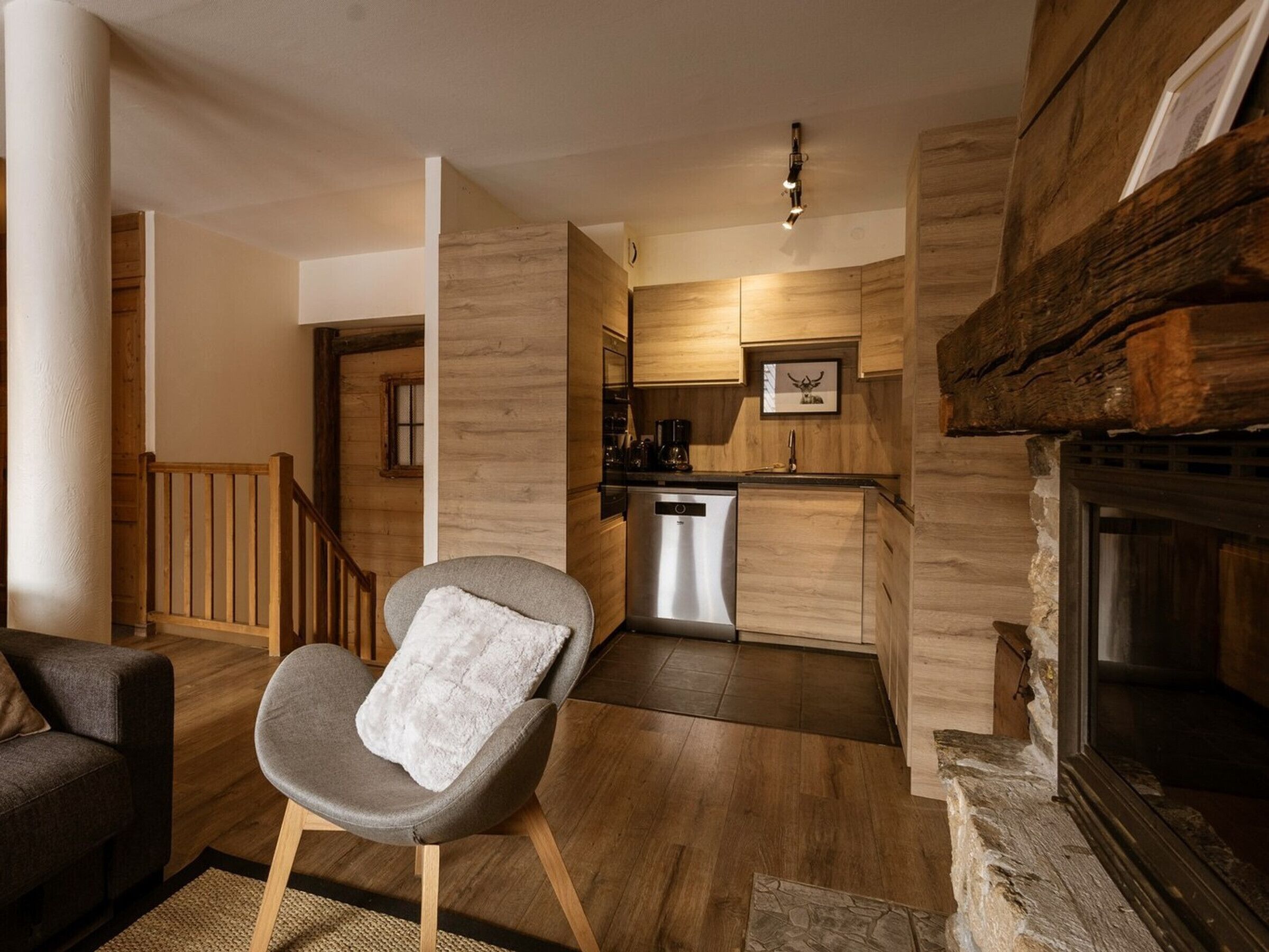 A modern living room with a grey armchair, wooden flooring, and a fireplace.