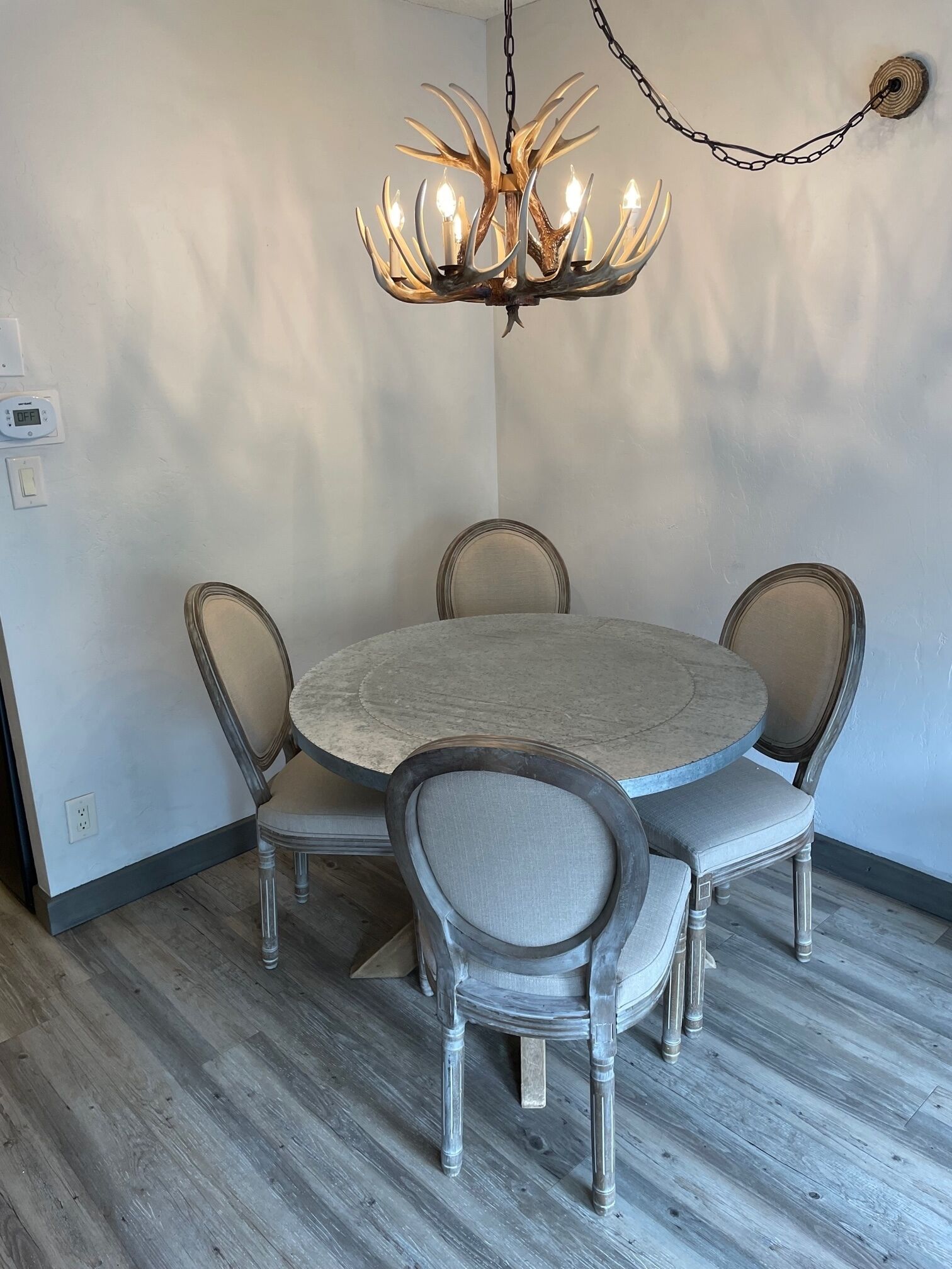 Ein Essbereich mit einem runden Tisch, sechs Stühlen, einer Kronleuchter mit Geweih-Design und einem Holzboden.
