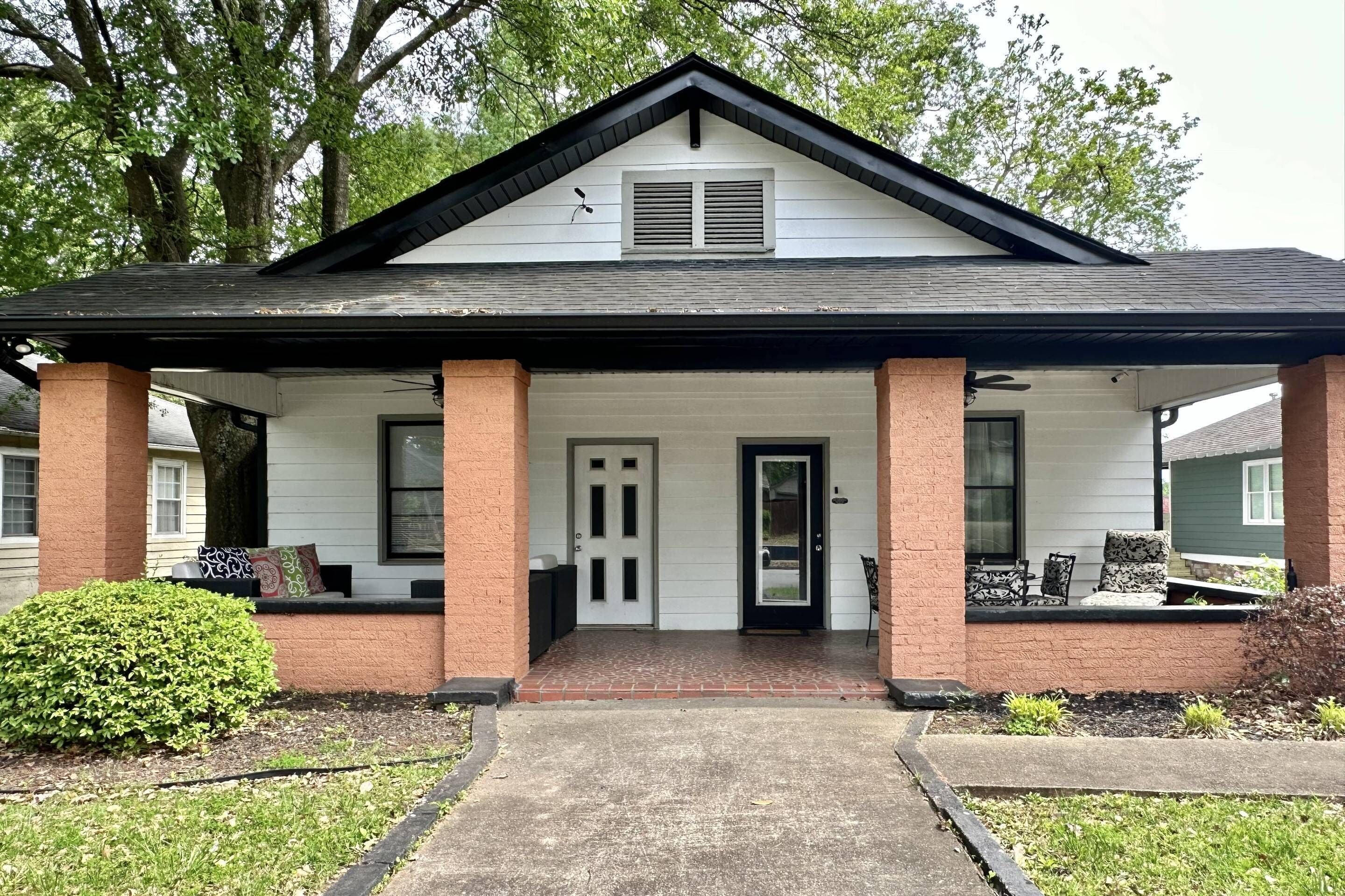 A two-story house with a front porch, a black roof, and a brick facade.