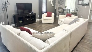 Una sala de estar moderna con un sofá seccional, un televisor de pantalla plana y un comedor con sillas y una mesa.
