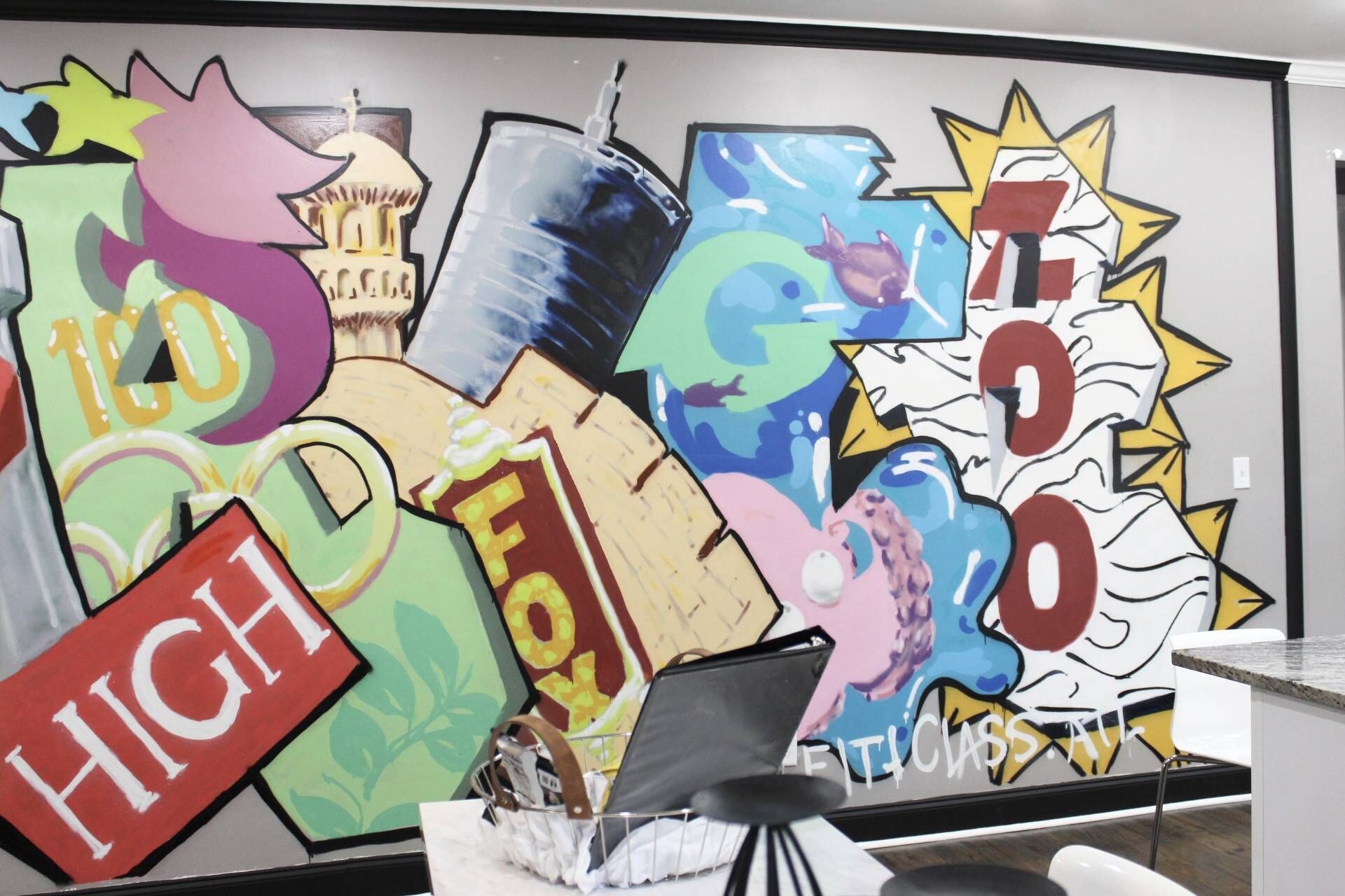 A colorful graffiti wall with various shapes and letters, a laptop on a desk, and a chair.