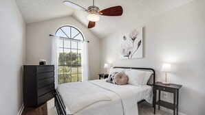 Een slaapkamer met een bed, nachtkastjes, een dressoir, een plafondventilator en een groot raam.
