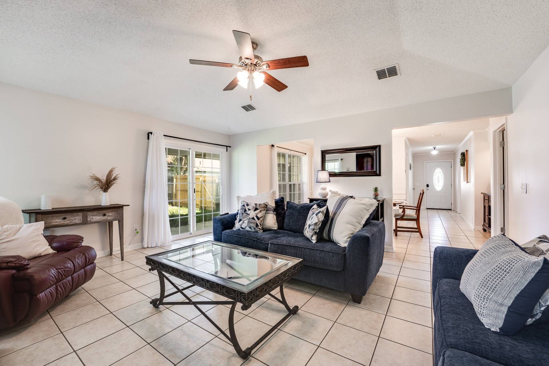 A spacious living room with a glass coffee table, a dark blue sofa, and a leather couch.