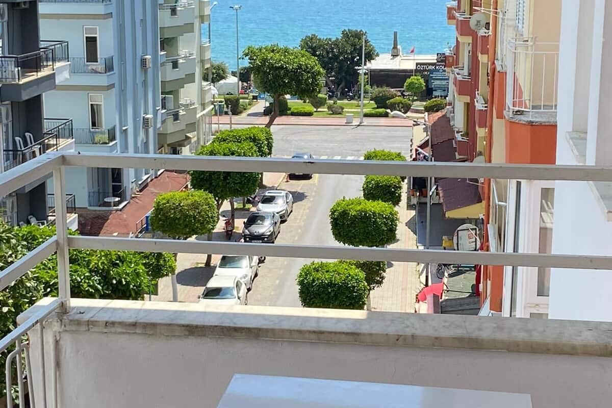 A balcony with a view of a coastal street, featuring multi-story buildings, parked cars, and a clear blue sky.
