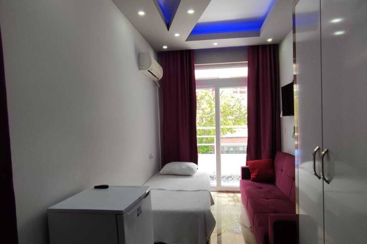 A modern hotel room with a bed, a small desk, a sofa, and a wardrobe.