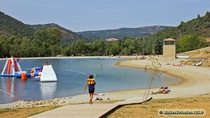 Une zone au bord du lac comprenant des jeux d’eau gonflables, une plage de sable et une tour en pierre.