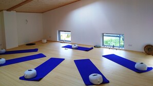 Une pièce spacieuse dotée de planchers en bois, de plusieurs tapis de yoga et de petits coussins blancs.