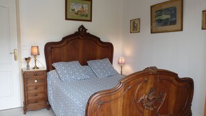Une chambre à coucher avec un lit en bois, deux tables de chevet avec des lampes, une commode et des tableaux encadrés accrochés au mur.