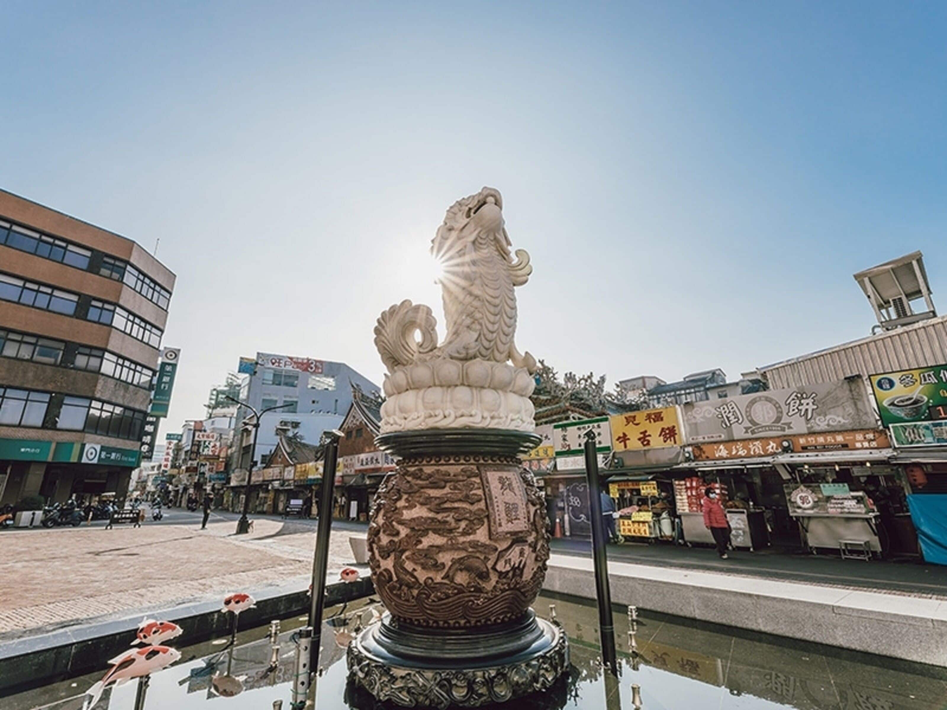 A traditional Chinese lion statue in a public square with modern buildings in the background.