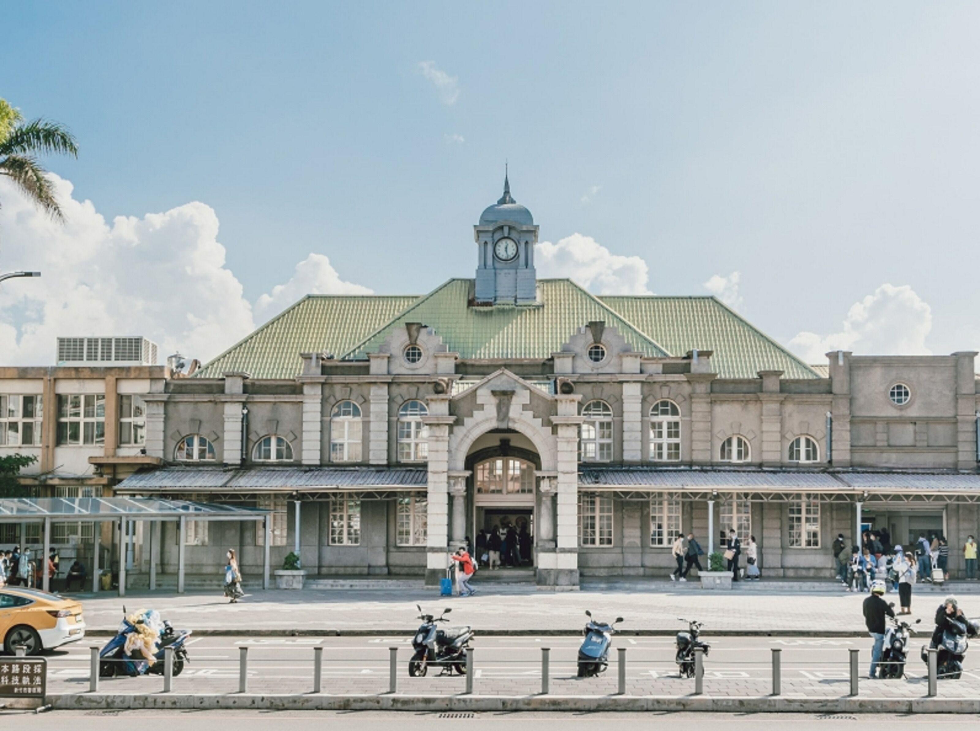 A large, historic building with a clock tower, featuring a central entrance with columns, and a green roof.
