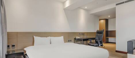 A modern hotel room with a large bed, a desk with a chair, a telephone, and a seating area with a chair.