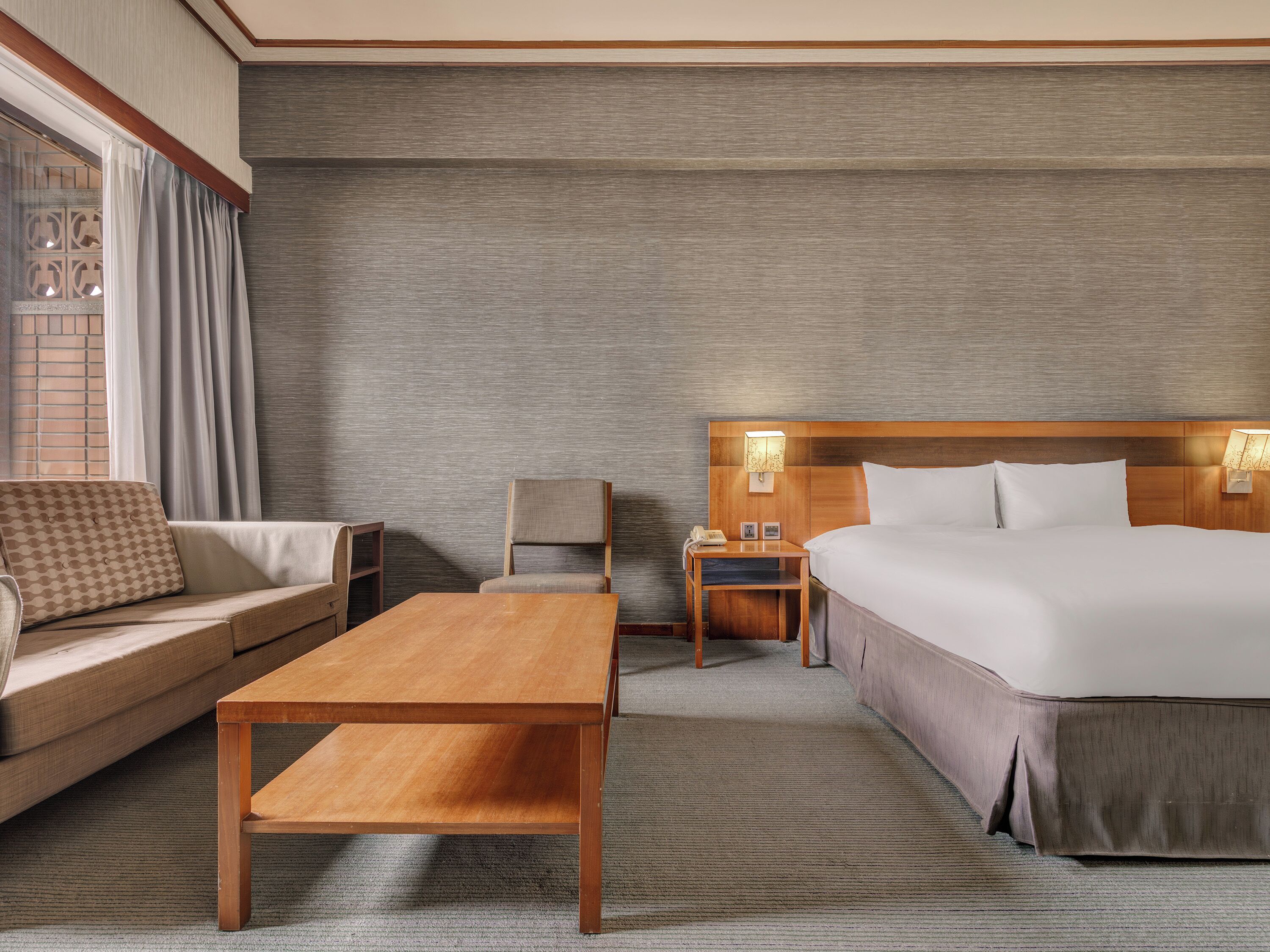 Una habitación de hotel con cama, sofá, mesa, silla y mesita de noche con lámpara.