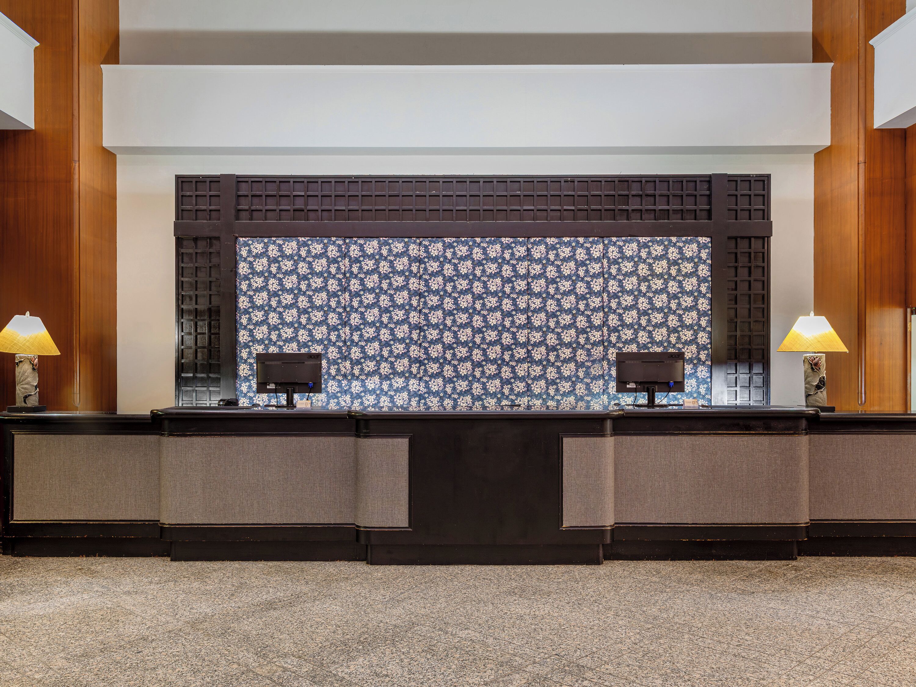 A reception desk with two lamps, a patterned wall, and a dark wooden panel.