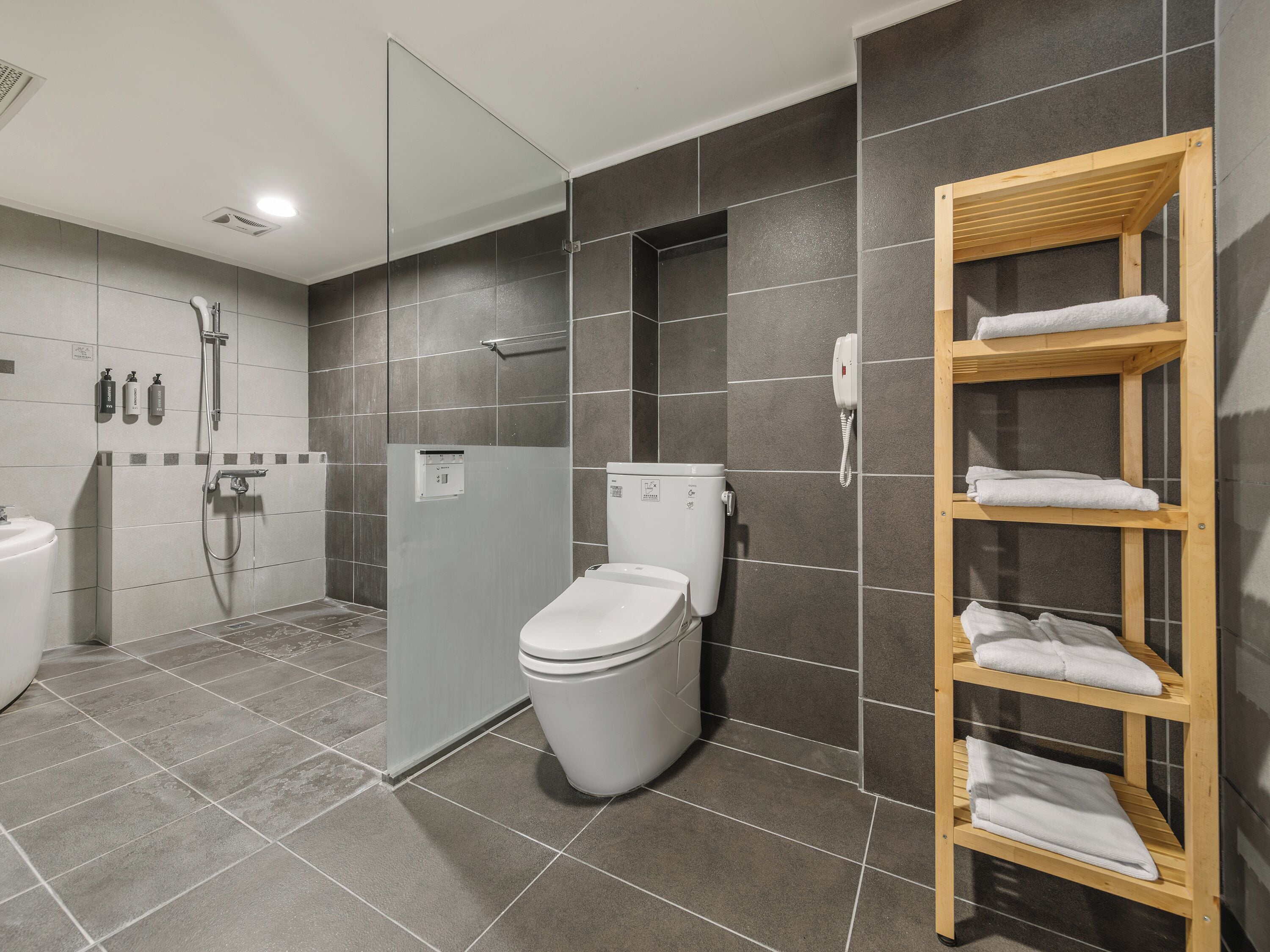 A modern bathroom with a shower, toilet, and a shelf with towels.