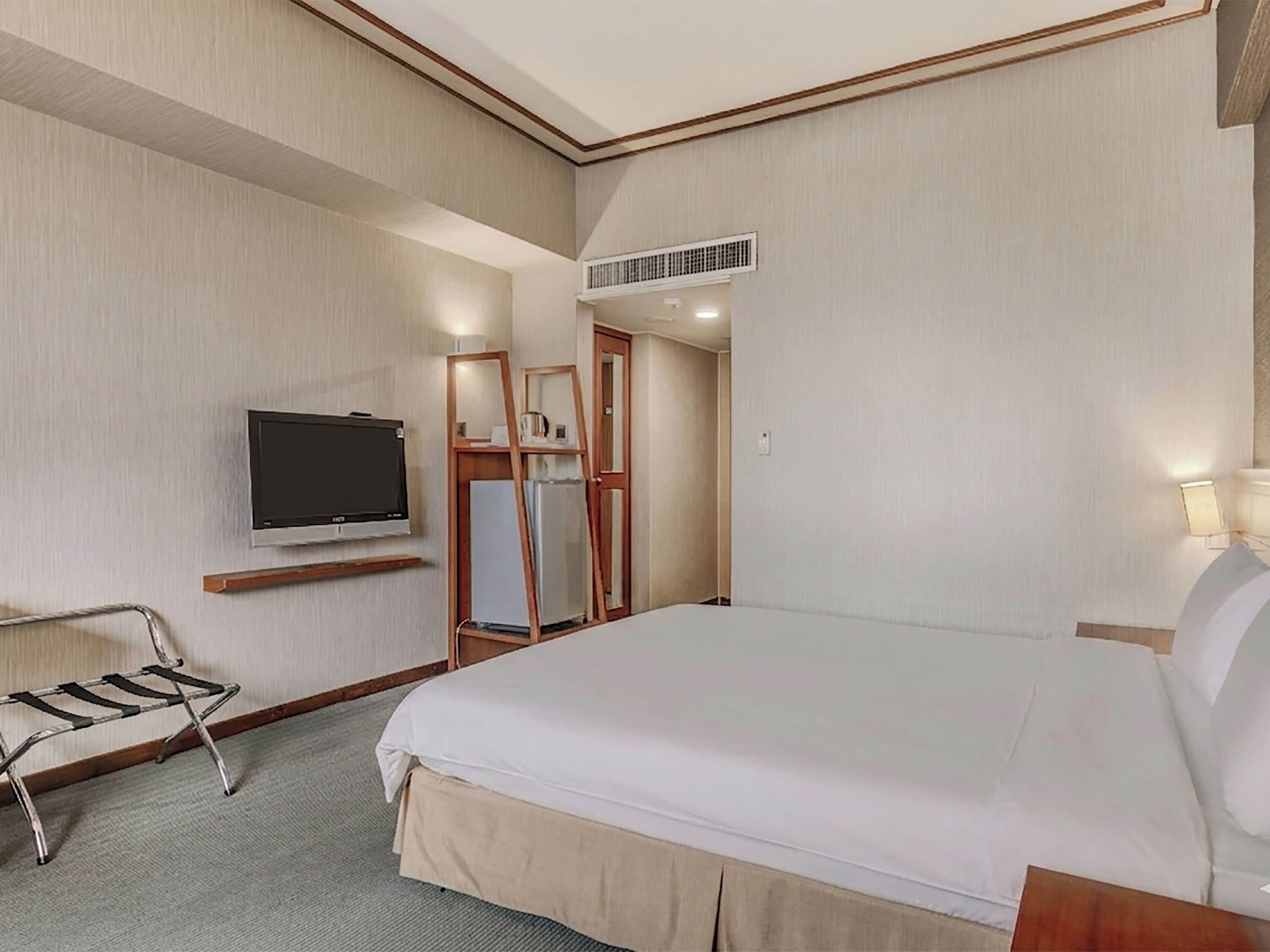 A hotel room with a bed, a television, a wardrobe, and a mirror.