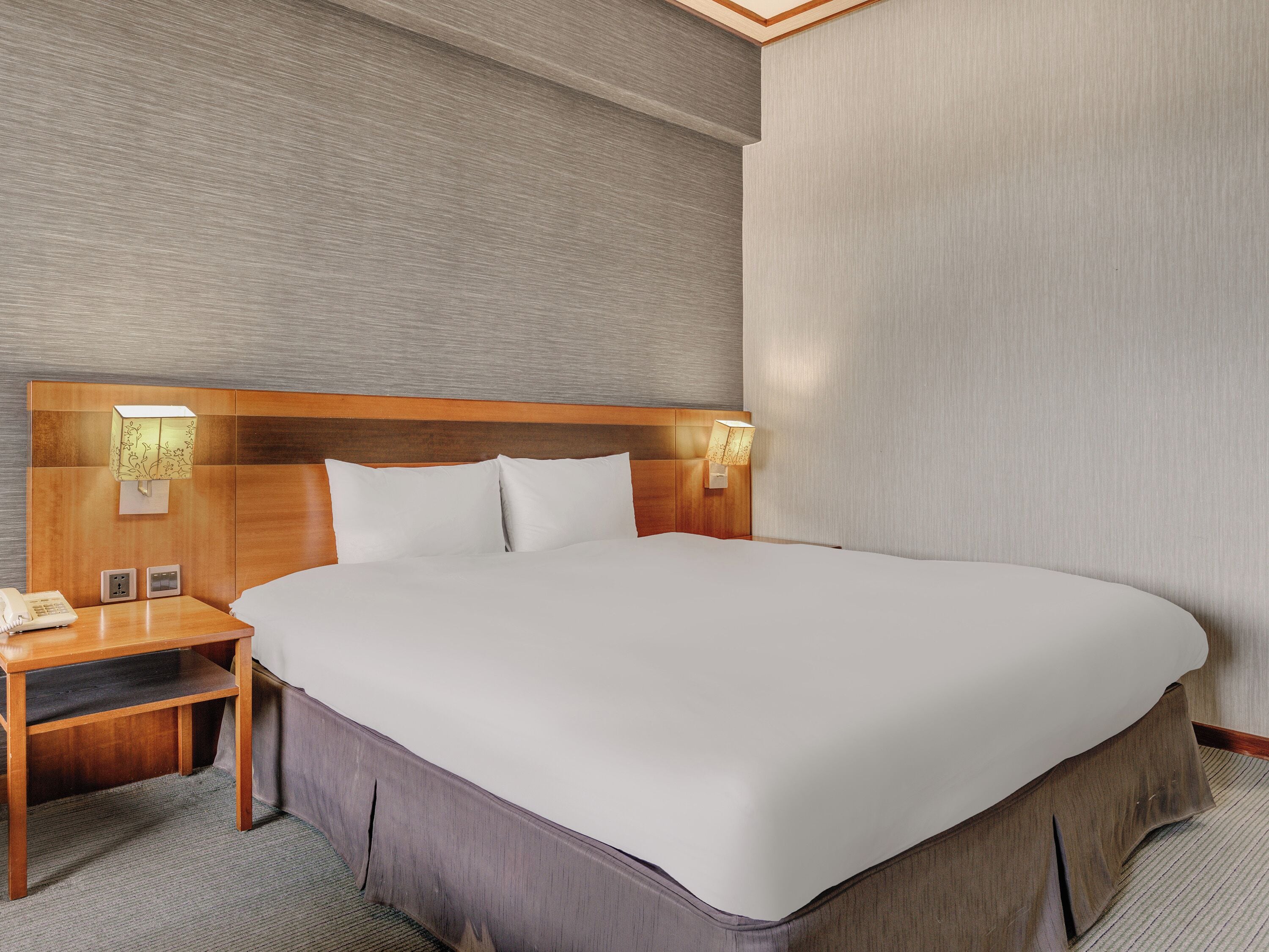 A hotel room with a large bed, wooden headboard, bedside lamps, a nightstand, and a telephone.