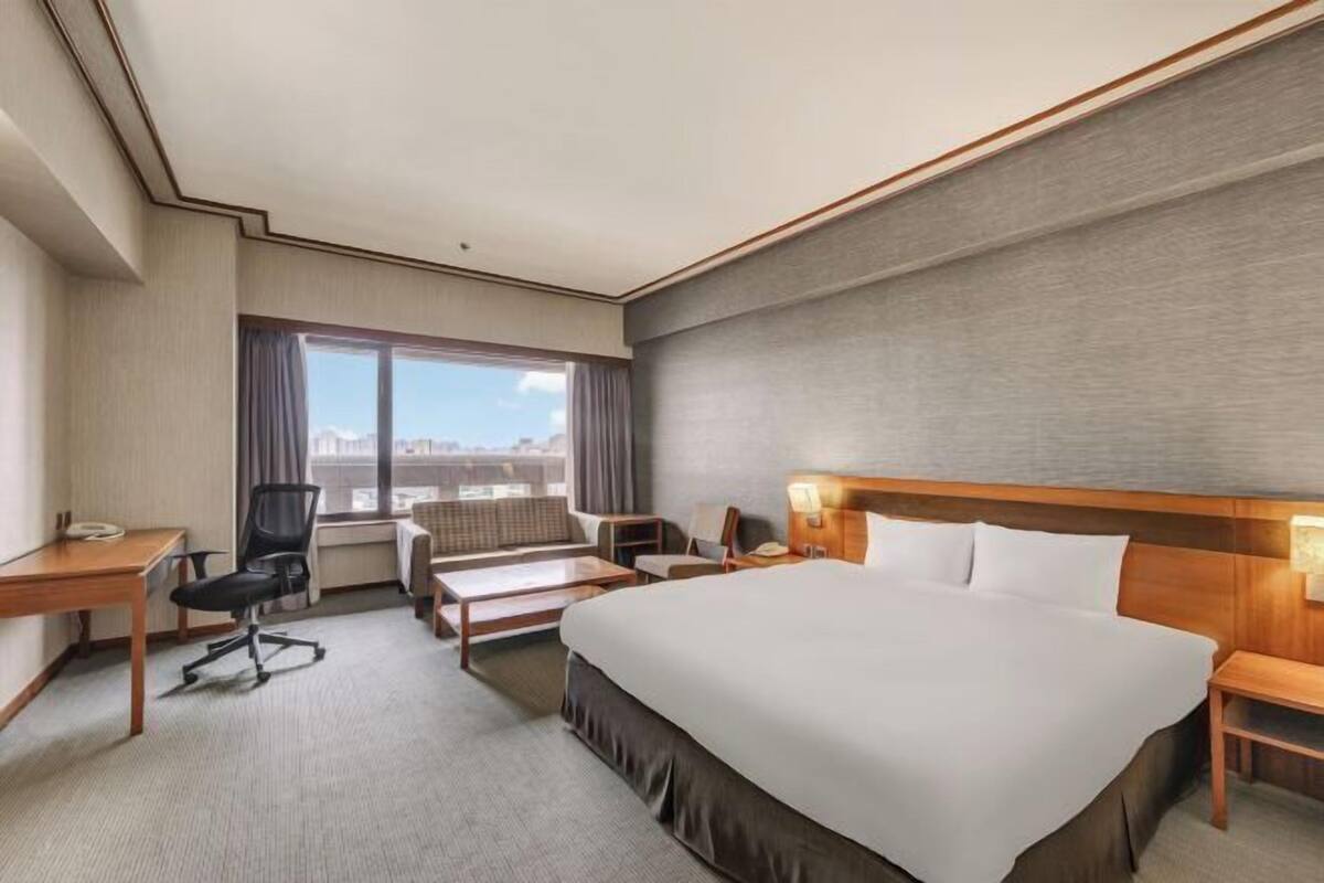 A hotel room with a large bed, a desk, a chair, a sofa, and a window with curtains.