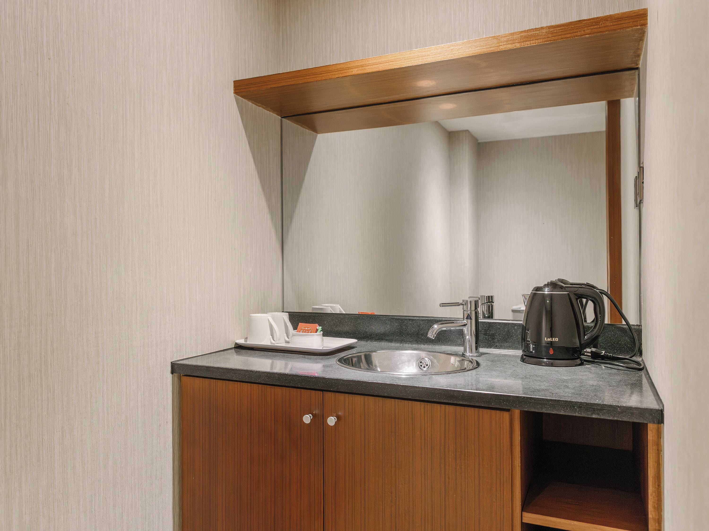 A modern bathroom with a wooden vanity, a sink, a mirror, and a coffee maker.