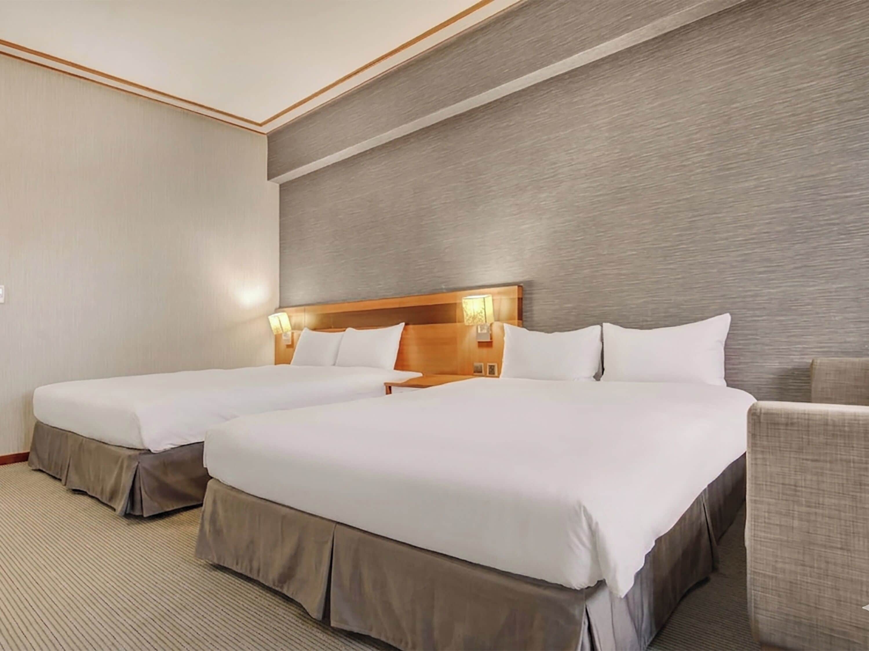 A hotel room with two beds, a wooden headboard, a light-colored carpet, and a small armchair.