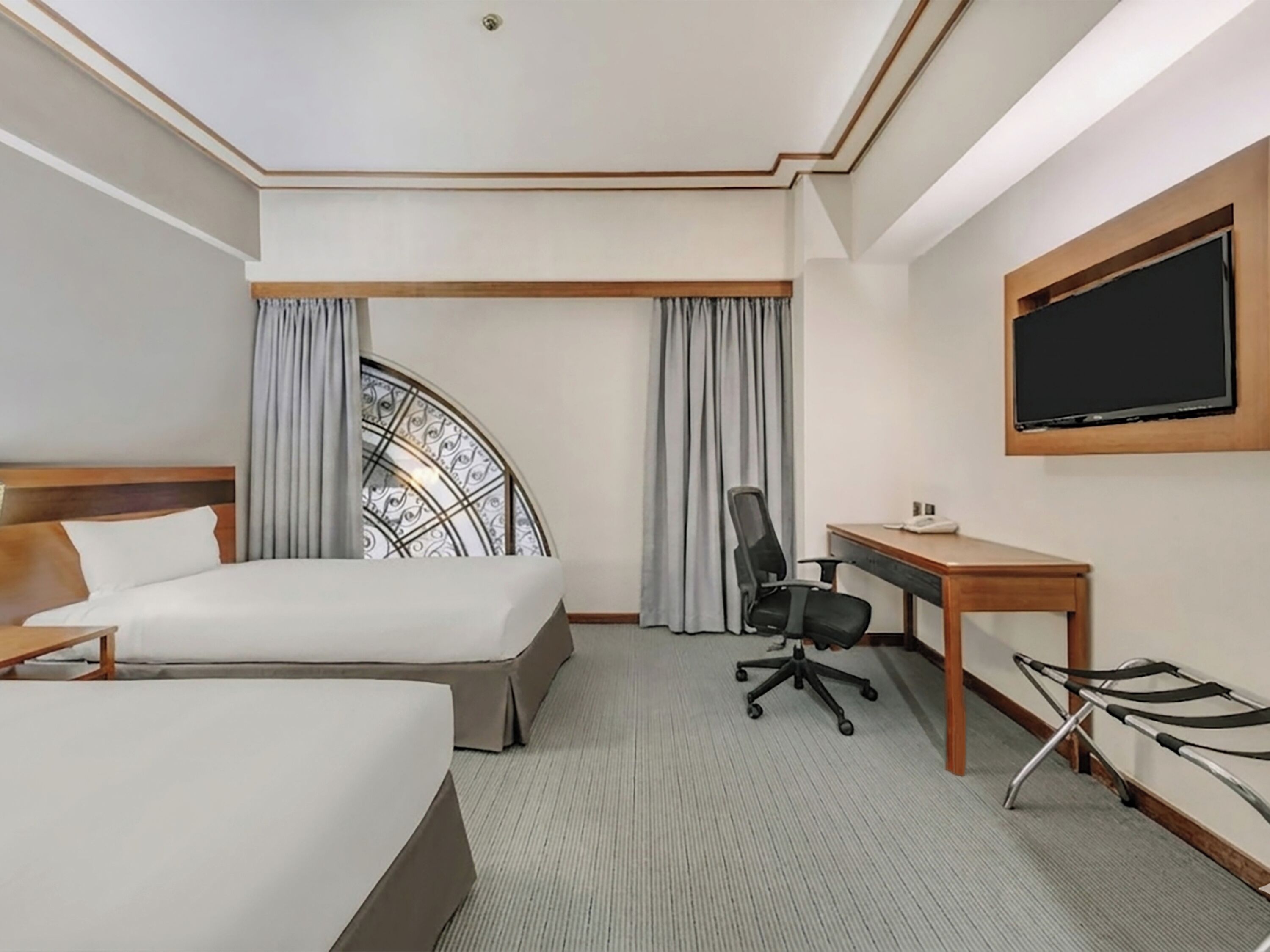 A hotel room with two beds, a desk, a chair, a TV, and a window with curtains.