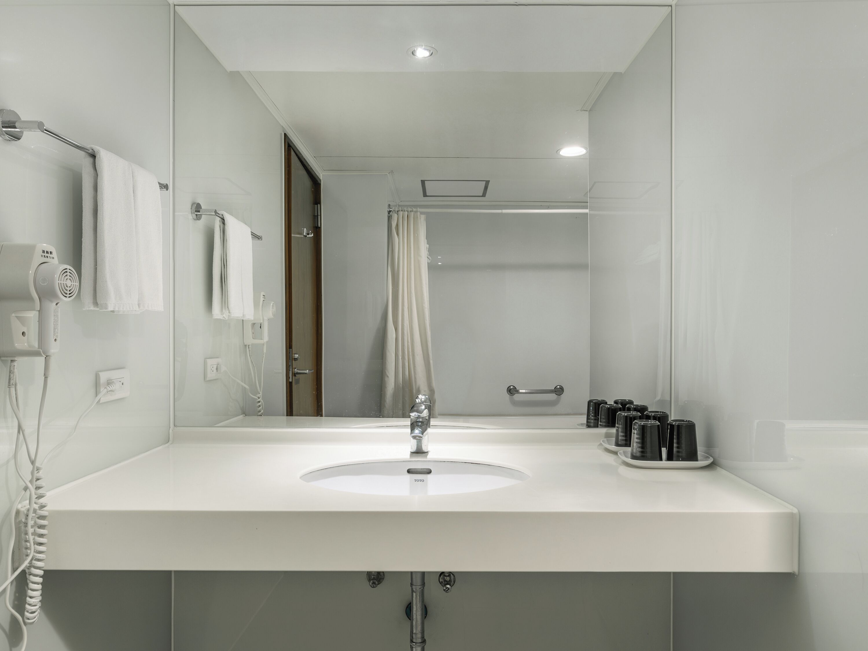 Un bany modern amb un lavabo blanc, un assecador de cabells portàtil i una cortina de bany.