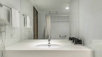 Un bany modern amb un lavabo blanc, un assecador de cabells portàtil i una cortina de bany.