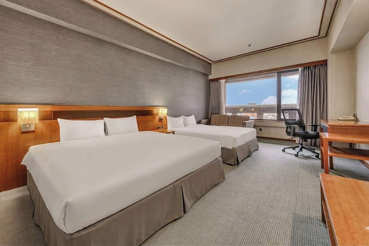 A hotel room with two beds, a desk, a chair, and a large window with a city view.
