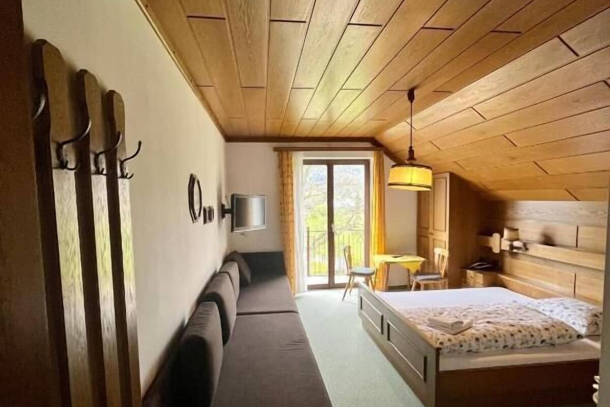 Una habitación con techo de madera, una cama, un sofá, un televisor y una ventana.