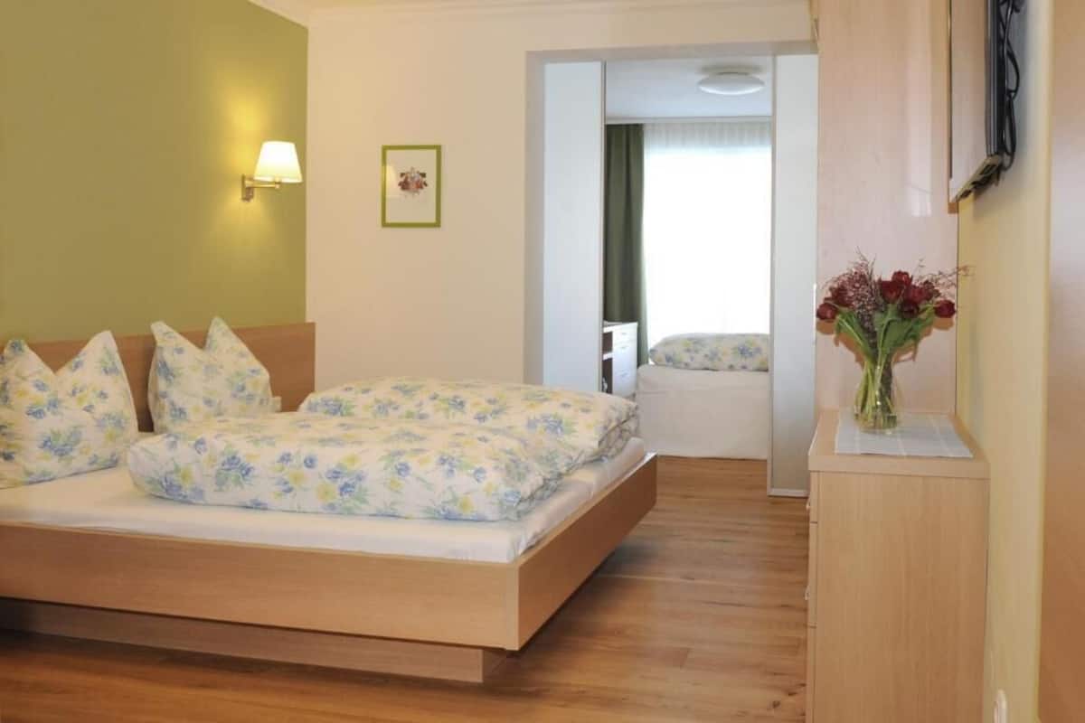 Un dormitorio con cama, una mesita de noche, una lámpara de pared y una puerta que da a otra habitación.