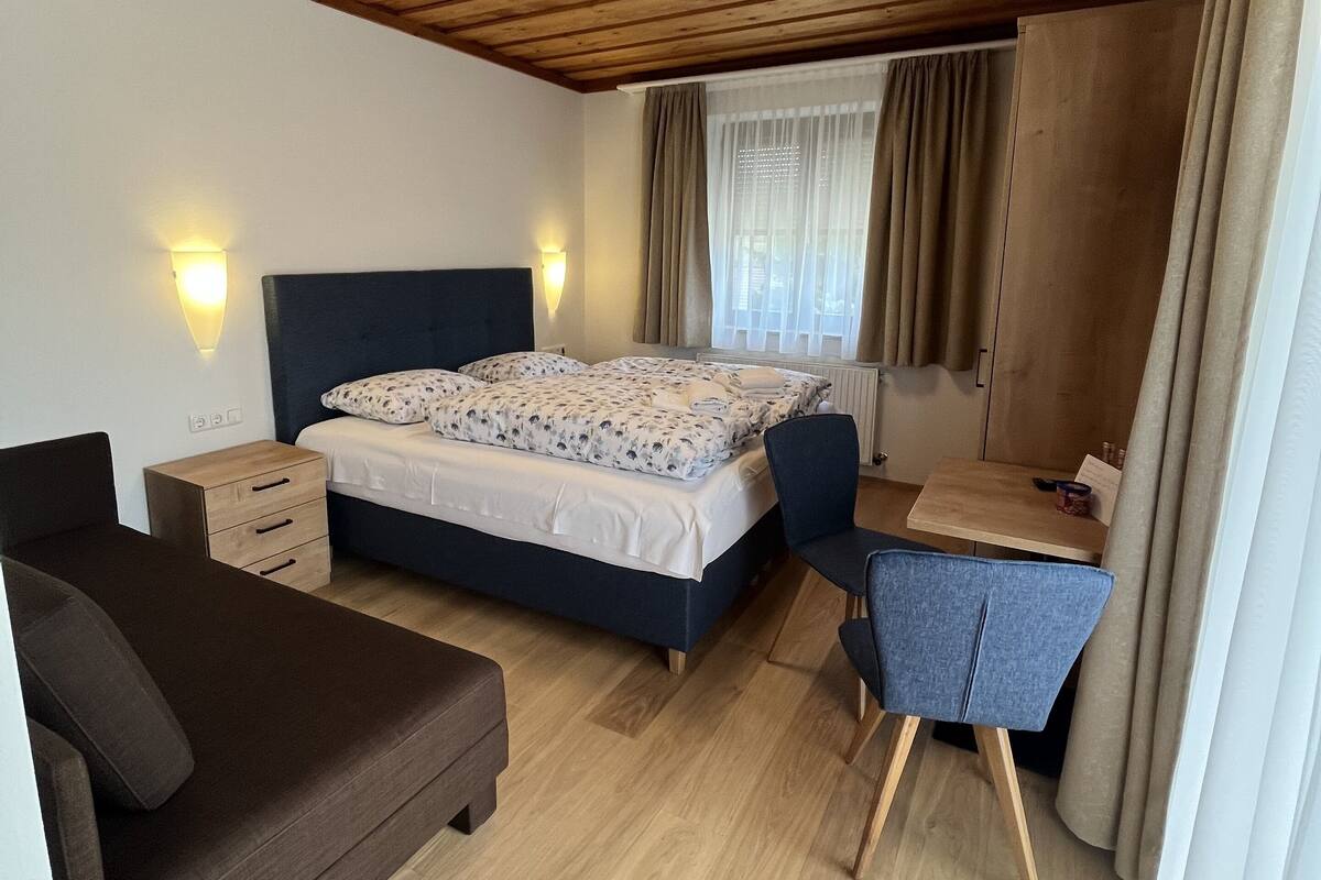 Un dormitorio con una cama, un escritorio, una silla, un aparador y un sofá.